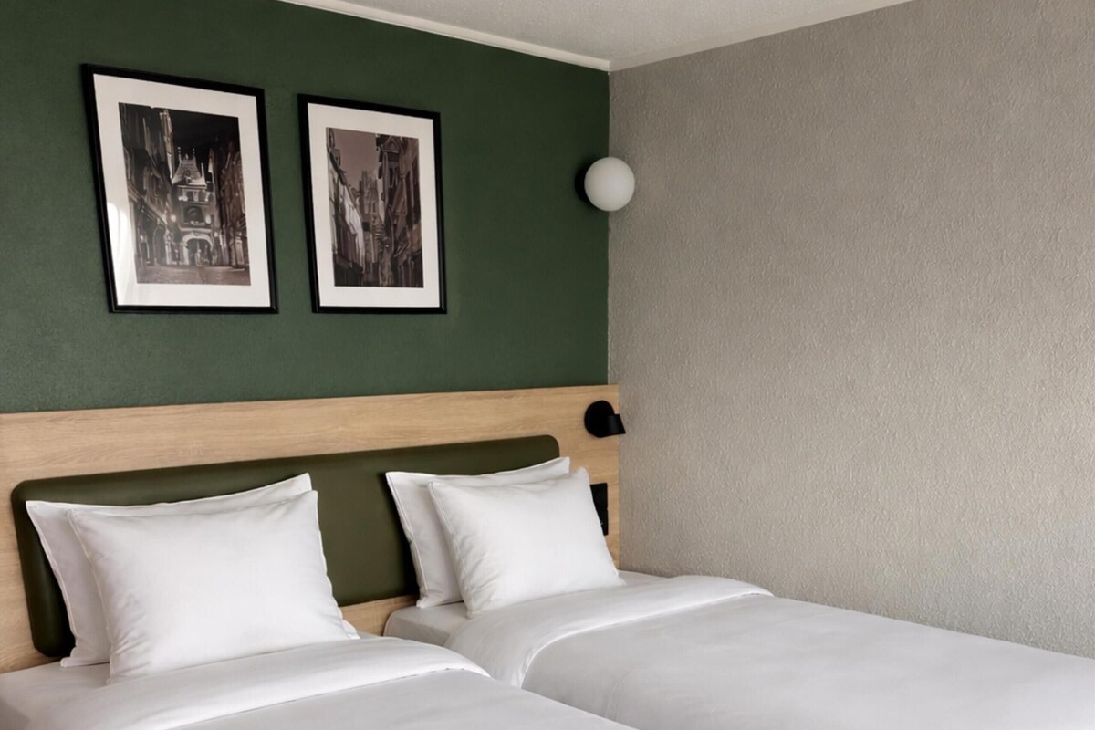 Un lit double avec du linge de lit blanc, une tête de lit en bois et deux tableaux encadrés accrochés au mur.