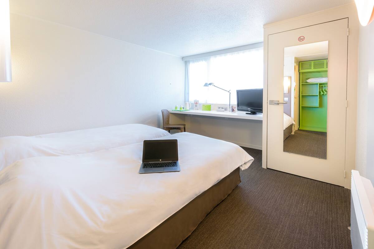 A hotel room with a bed, a desk with a laptop, a TV, and a green closet.