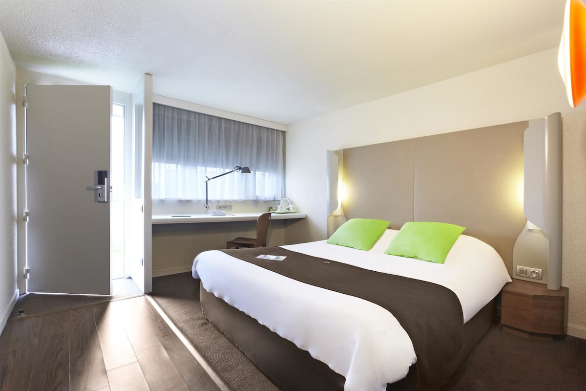 A hotel room with a bed, bedside tables, a desk, and a window with curtains.