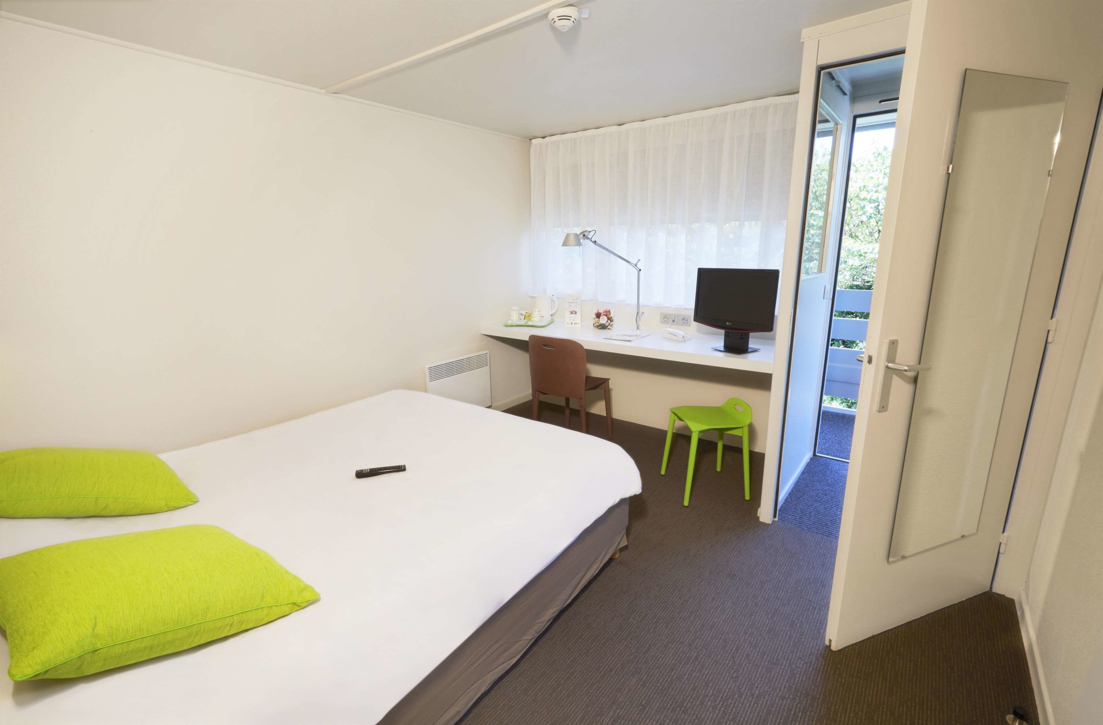 Habitación de hotel con cama, escritorio, silla, computadora y puerta que da a un espacio exterior.