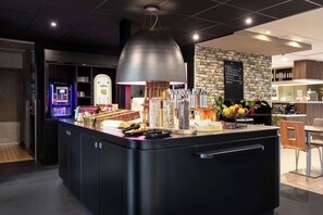 A modern bar area with a central island, a digital menu board, and a variety of bar tools and condiments. - Campanile Bethune Fouquieres (Fouquieres-les-Bethune)