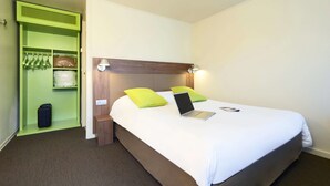 A hotel room with a bed, a laptop, a green storage unit, and a wooden headboard. - Campanile Bethune Fouquieres (Fouquieres-les-Bethune)