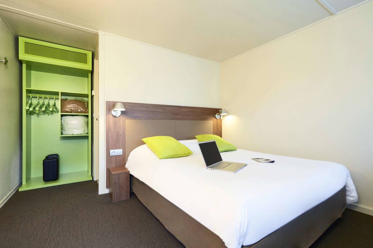A hotel room with a bed, a laptop, a green storage unit, and a wooden headboard.