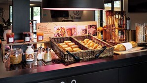 A breakfast buffet with baskets of pastries, condiments, and a sign advertising a small breakfast. - Campanile Bethune Fouquieres (Fouquieres-les-Bethune)
