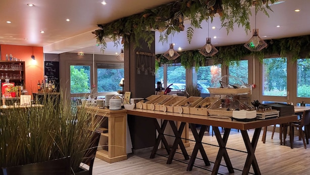 A restaurant with a wooden counter, hanging plants, and a view of trees through large windows. - KYRIAD ROUEN NORD - Mont-Saint-Aignan (Mont-Saint-Aignan)