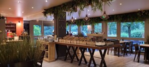 A restaurant with a wooden counter, hanging plants, and a view of trees through large windows. - KYRIAD ROUEN NORD - Mont-Saint-Aignan (Mont-Saint-Aignan)