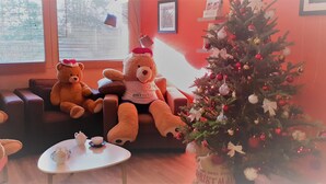 A room with three teddy bears seated on a couch, a small table with a teapot and cup, and a Christmas tree decorated with ornaments. - KYRIAD ROUEN NORD - Mont-Saint-Aignan (Mont-Saint-Aignan)