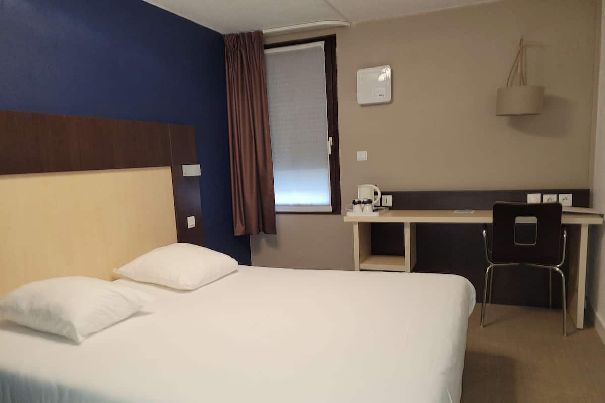 A hotel room with a bed, a desk, and a chair.
