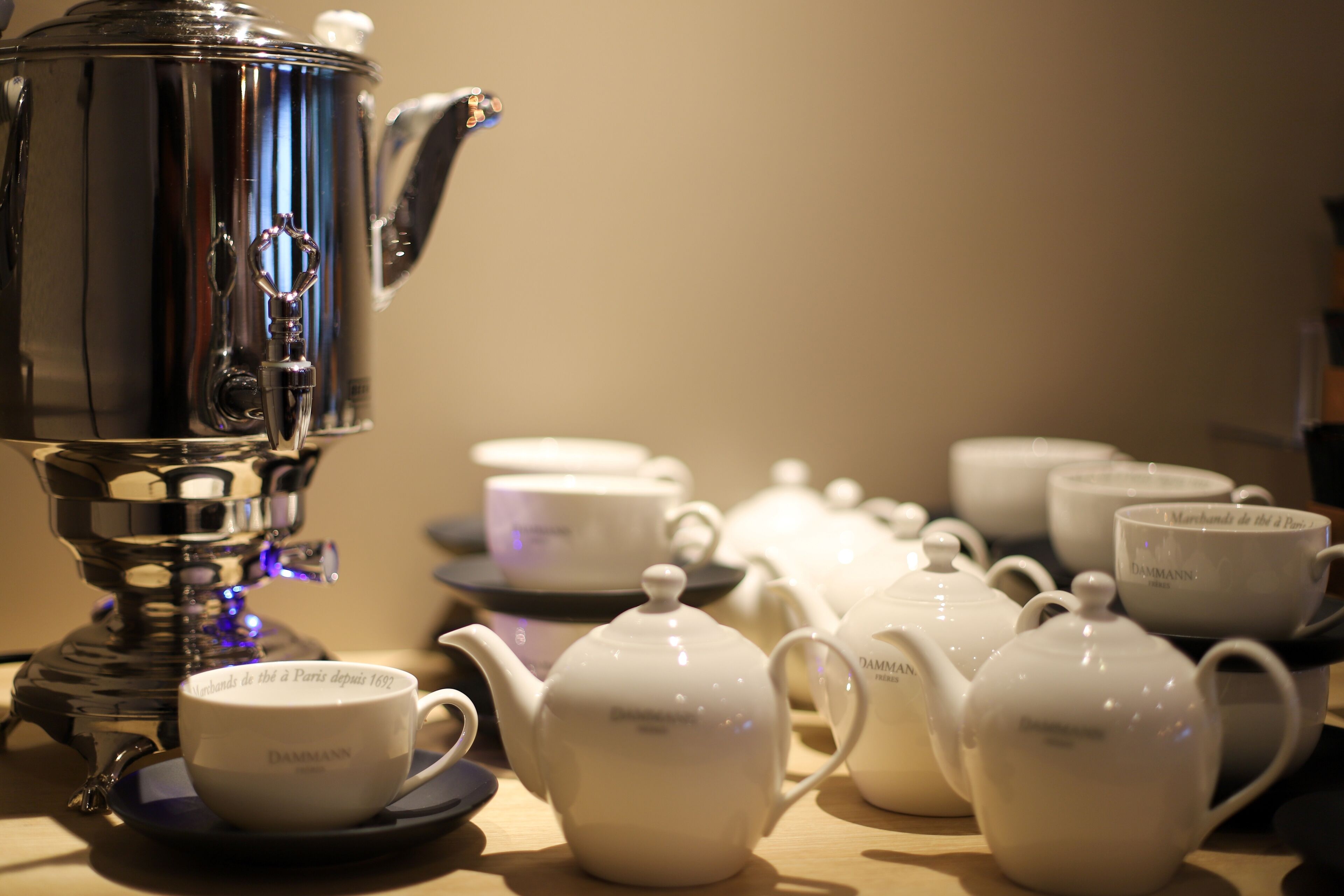 A coffee station with a coffee maker, teapots, cups, and saucers.