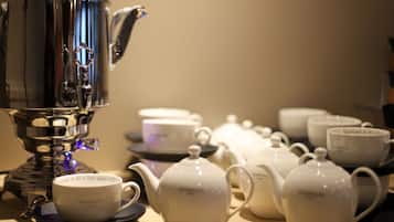A coffee station with a coffee maker, teapots, cups, and saucers.