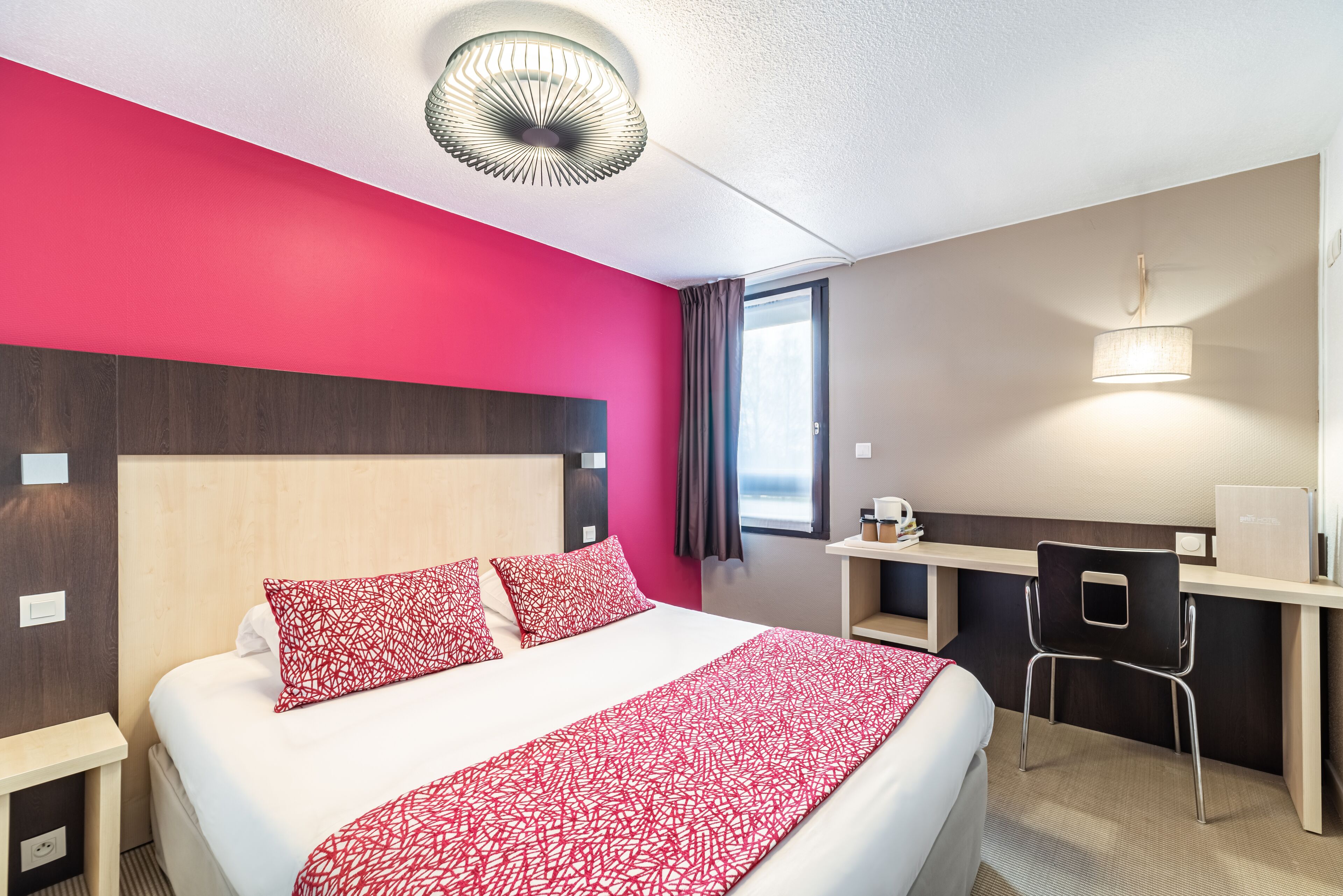 Una habitación de hotel con una cama, un escritorio, una silla y una ventana.