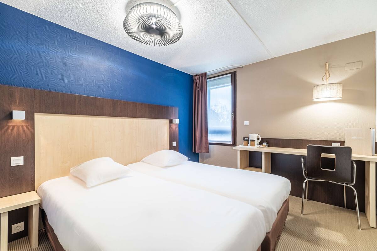 A hotel room with two beds, a desk, and a chair.