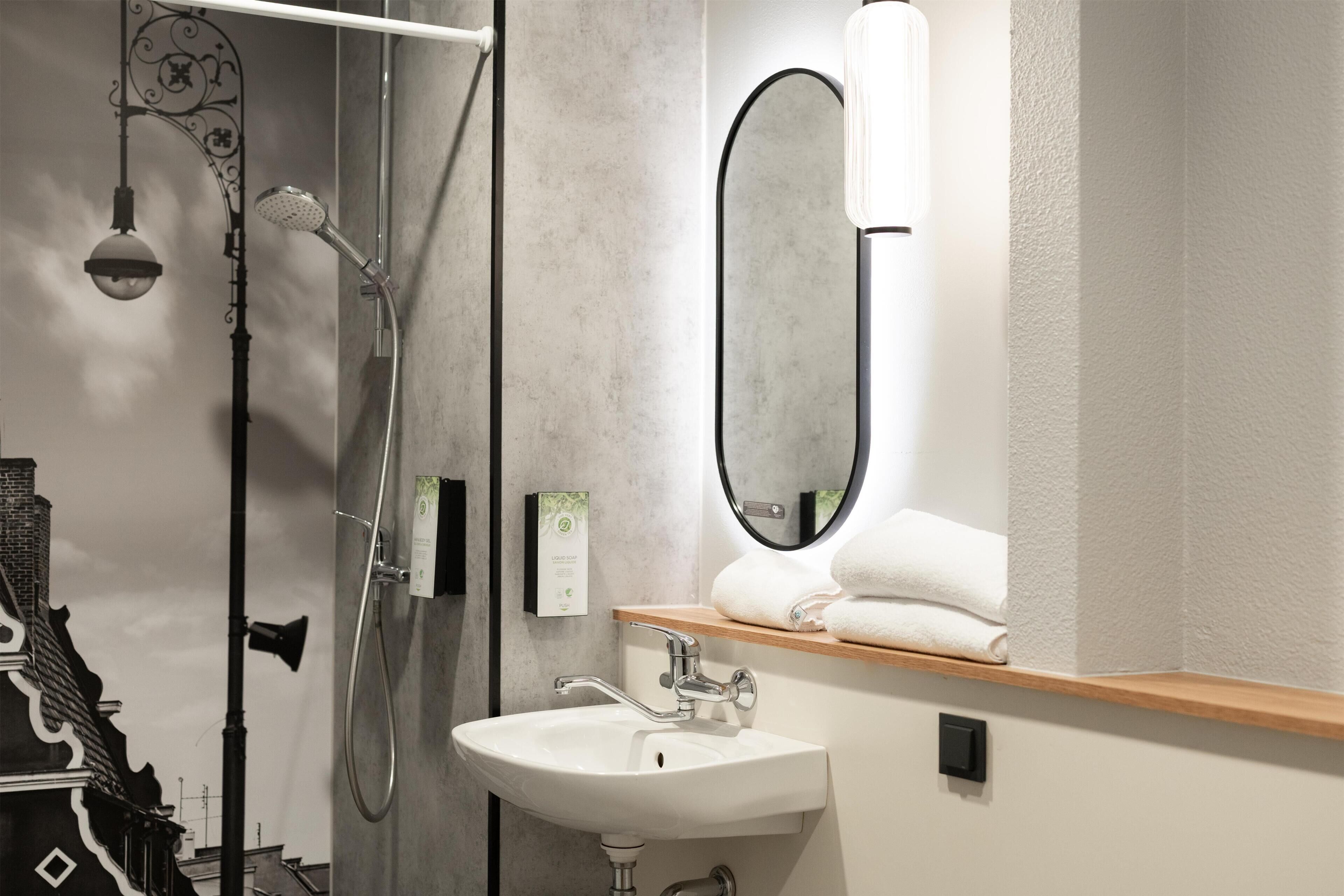 A bathroom with a white sink, a mirror, a shower, and a towel rack.