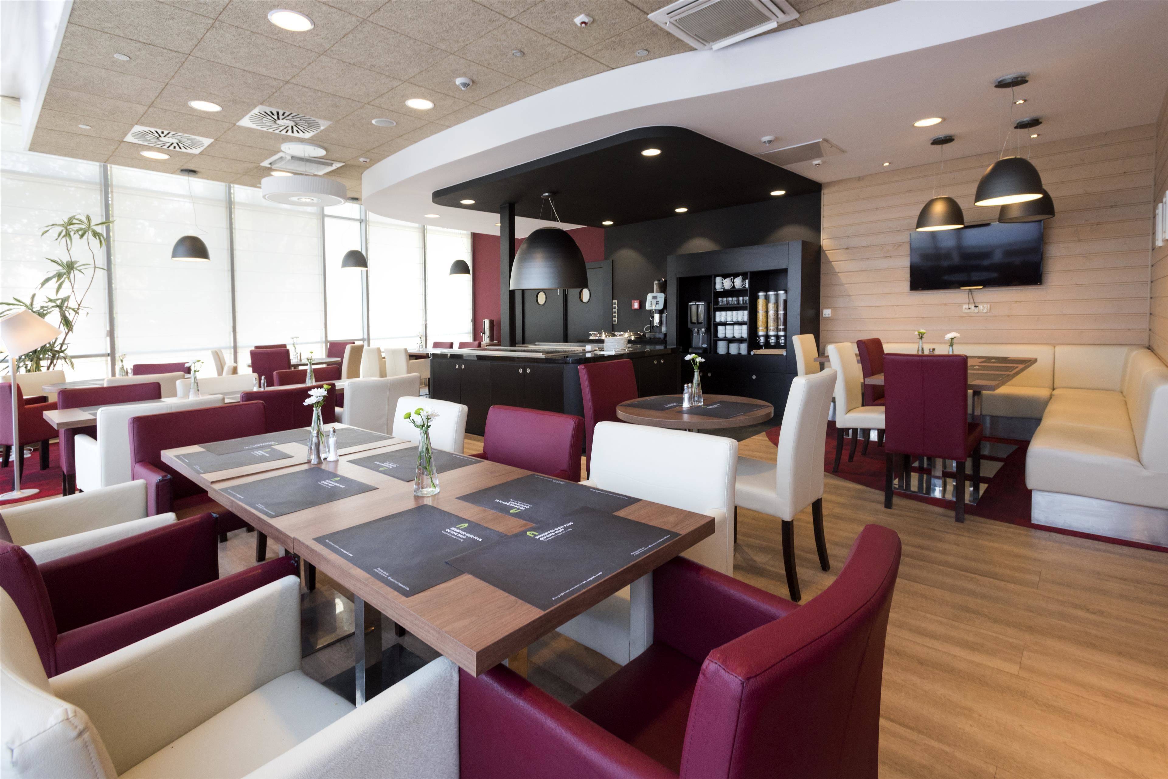 A modern restaurant with a mix of red and white seating, a central bar area, and a flat-screen TV mounted on the wall.