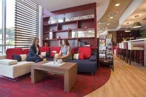A modern hotel lobby with red sofas, a wooden coffee table, and a bookshelf filled with books and magazines. - Campanile PRIME - Wroclaw Stare Miastro (Wroclaw)