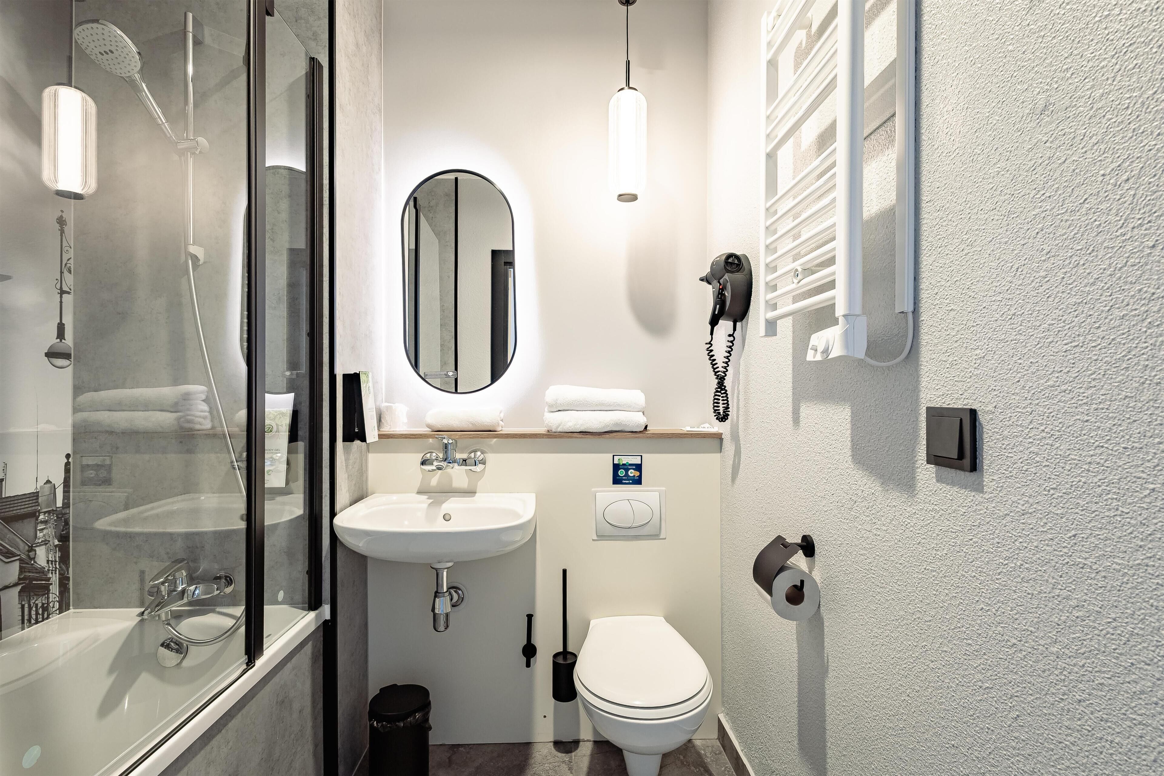 Un bany modern amb dutxa amb envàs de vidre, un lavabo, una tassa i un assecador de cabells fixat a la paret.