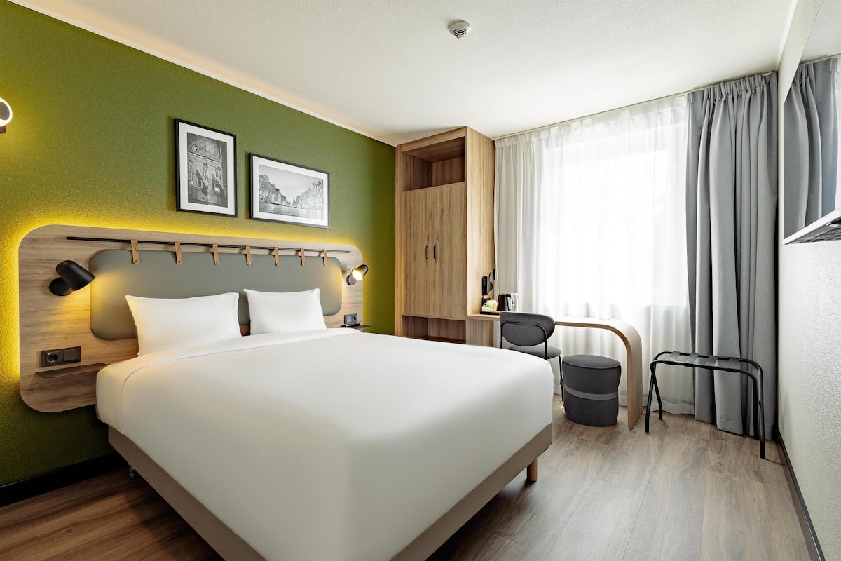 Habitación de hotel con cama, escritorio, silla y vistas al exterior.