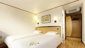 Habitación de hotel con dos camas, un armario de madera y aire acondicionado instalado en la pared.
