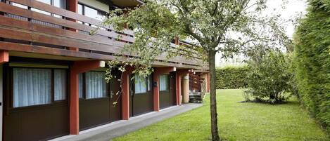 A modern building with a red facade, multiple windows, and a small tree in the front yard.