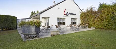 Un restaurante con fachada blanca, techo inclinado y un letrero con logotipo rojo y negro.