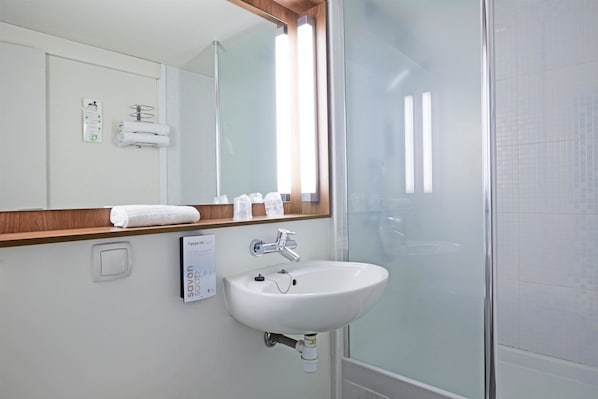 A modern bathroom with a white sink, a large mirror, and a glass shower enclosure.