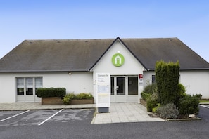 A building with a green logo, a signboard, and a parking area.