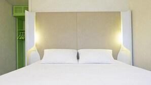 A double bed with two white pillows, a beige headboard, and two wall-mounted lamps on either side. - Campanile Lens (Lens)