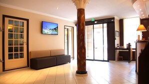 A lobby with a marble column, a sofa, a television, and a reception desk. - Hôtel Menton Riviera (Menton)