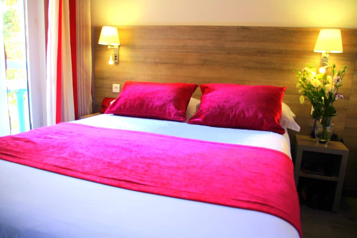 Una cama con una colcha blanca y rosa, dos almohadas rojas y dos lámparas de noche.