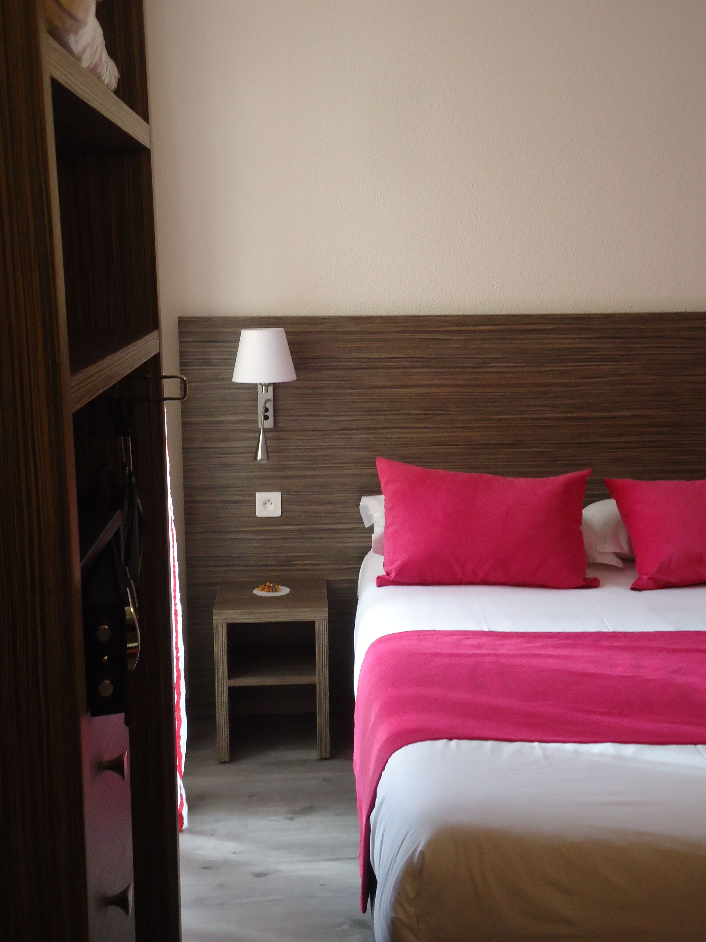 Una habitación de hotel con una cama, una mesita de noche, una lámpara y un armario.