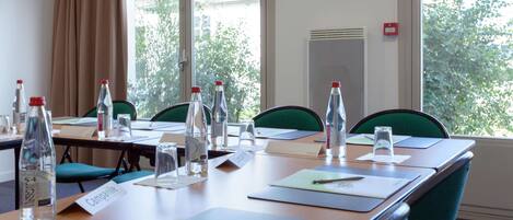 A conference room with a long table, chairs, name cards, water bottles, and a window with a view of trees.