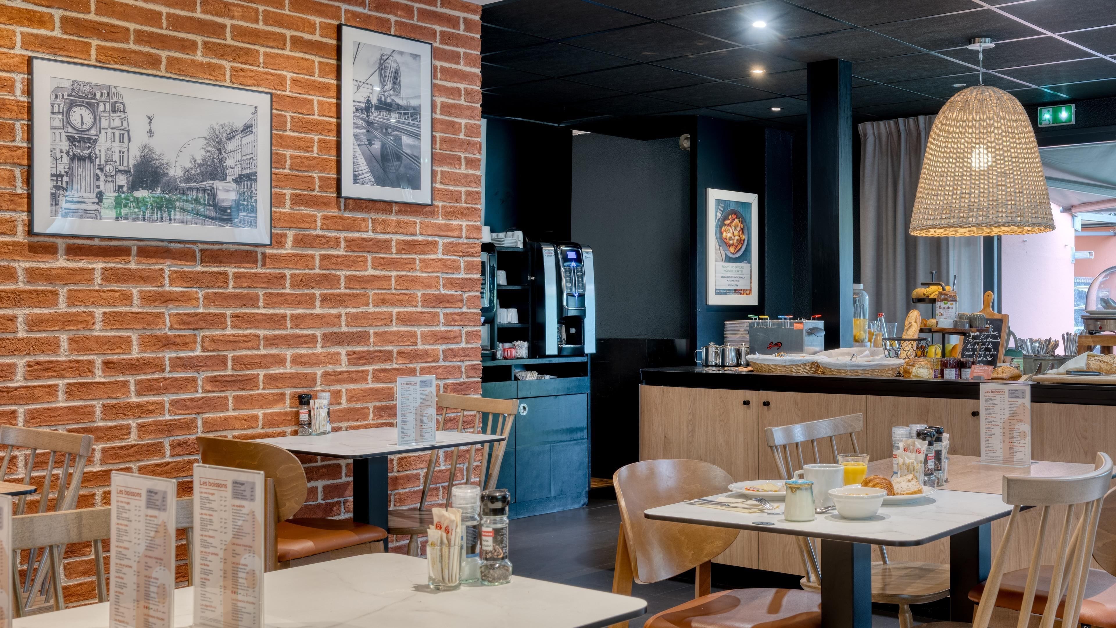Un restaurante con paredes de ladrillo, cuadros enmarcados, mesas con sillas, una barra con productos alimenticios y un candelabro colgante.