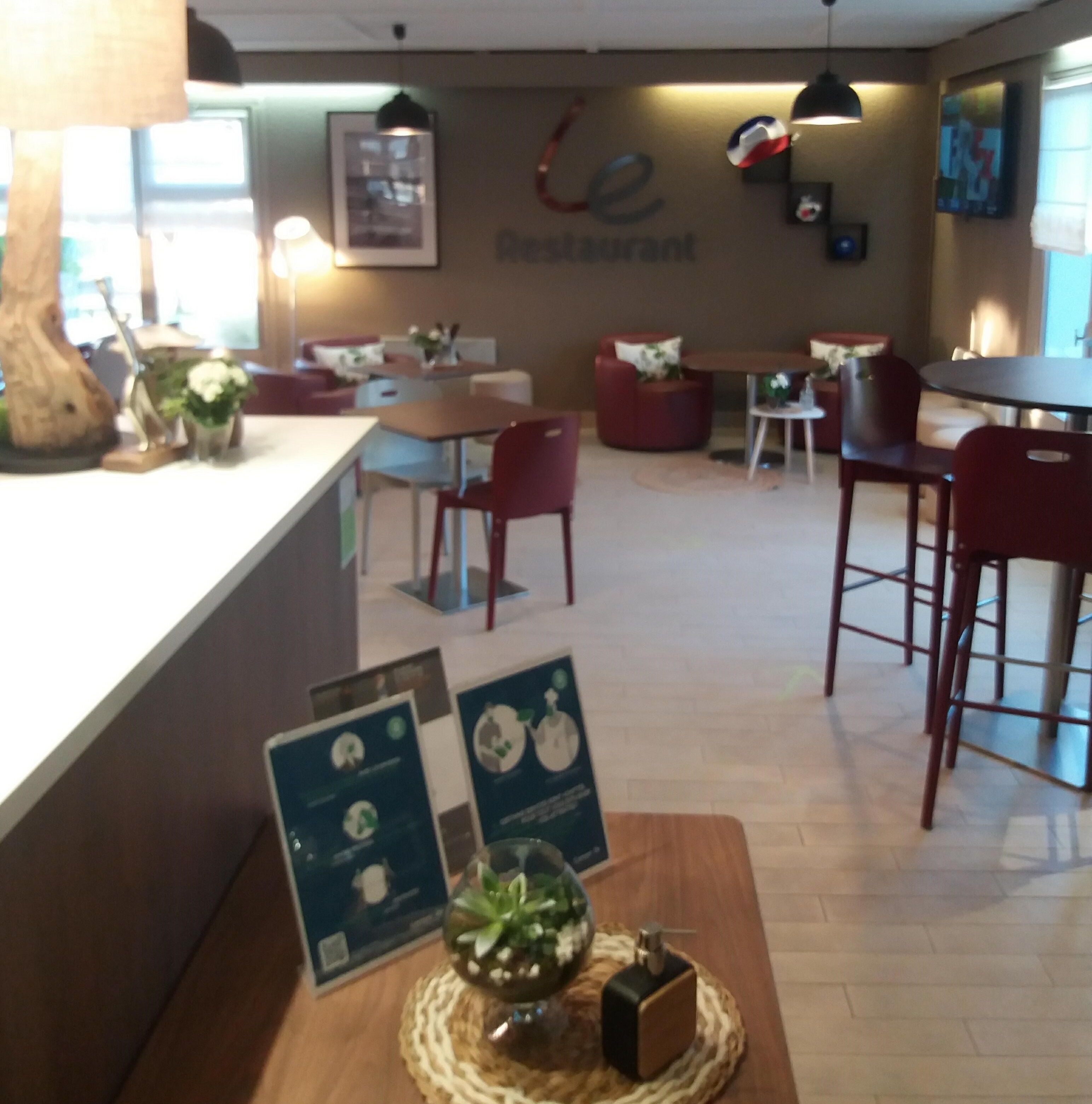 Interior de un restaurante con mostrador, zona de mesas y una pared con un letrero.
