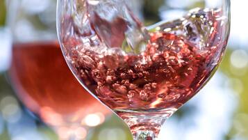 A glass being filled with a red liquid, likely wine, outdoors with a blurred background of greenery.