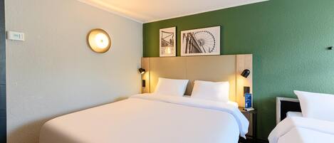 Habitación de hotel con una cama grande, dos mesitas de noche con lámparas, un reloj de pared y dos cuadros enmarcados.