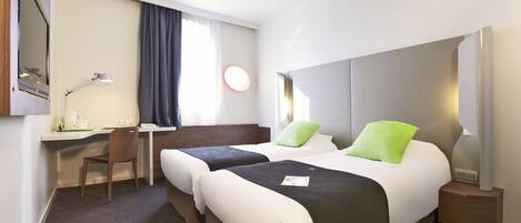 Une chambre d’hôtel avec deux lits, un bureau, une chaise et une table de chevet avec une lampe.
