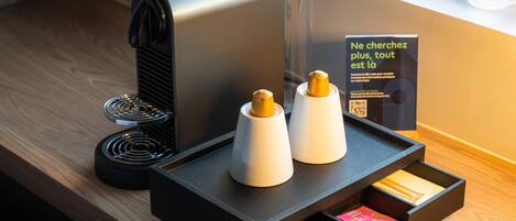 A modern coffee machine with a tray holding two coffee pods and a drawer with snacks.