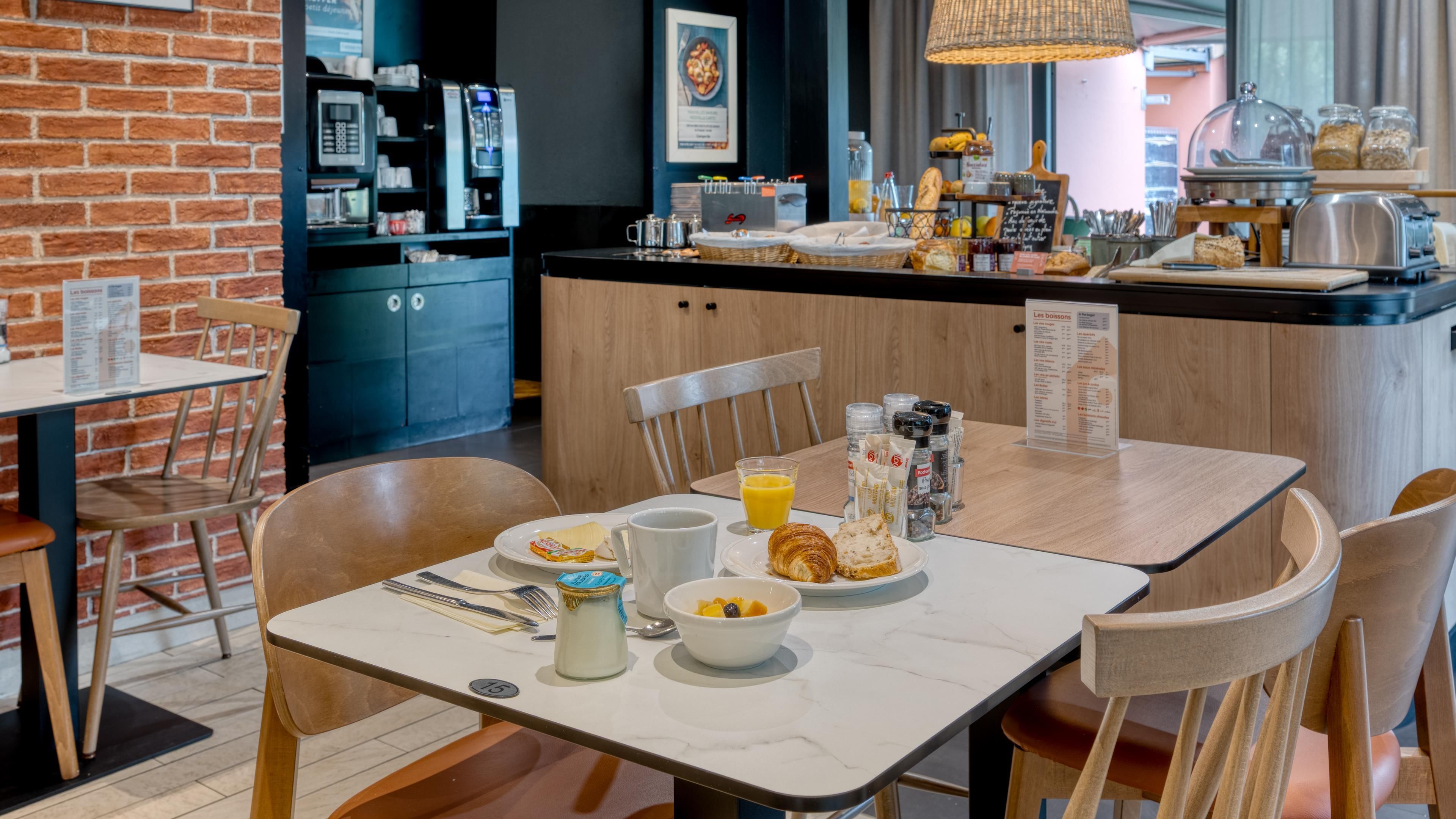 Un desayuno servido en una mesa con sillas, una cafetera y diversos alimentos.