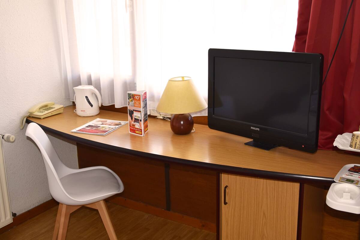 A hotel room desk with a computer monitor, a lamp, a telephone, and a chair.