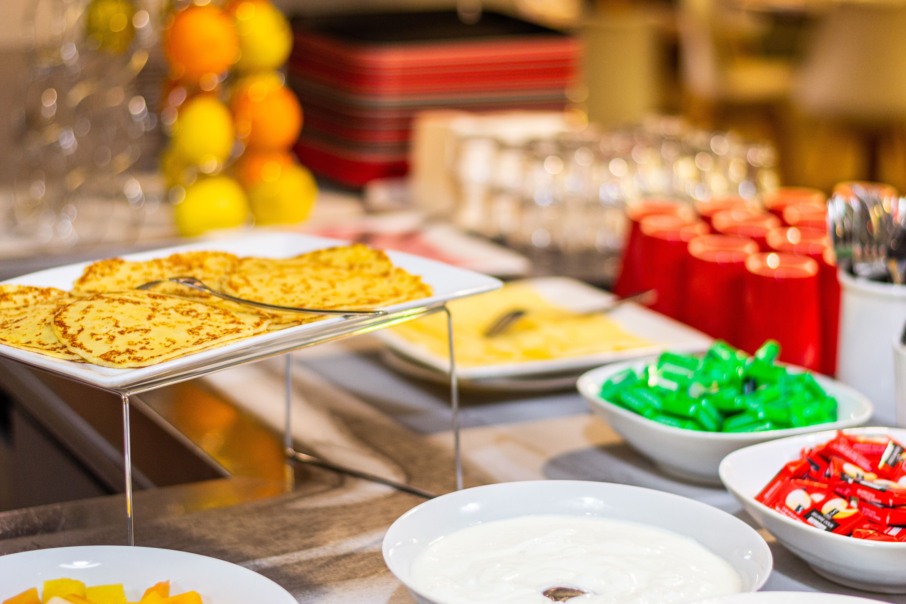 A buffet table with various food items including pancakes, fruit, and condiments.