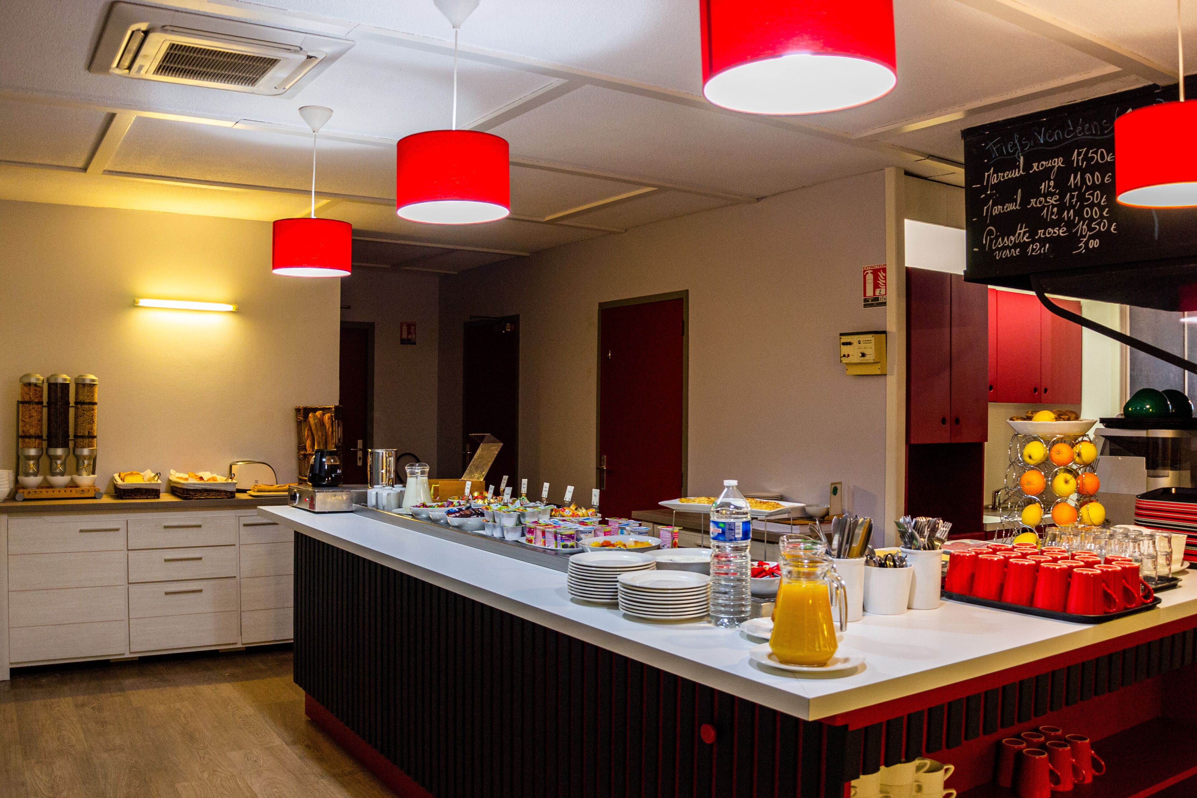 Disposição de buffet com diversos alimentos, um dispensador de água e um cardápio em lousa.