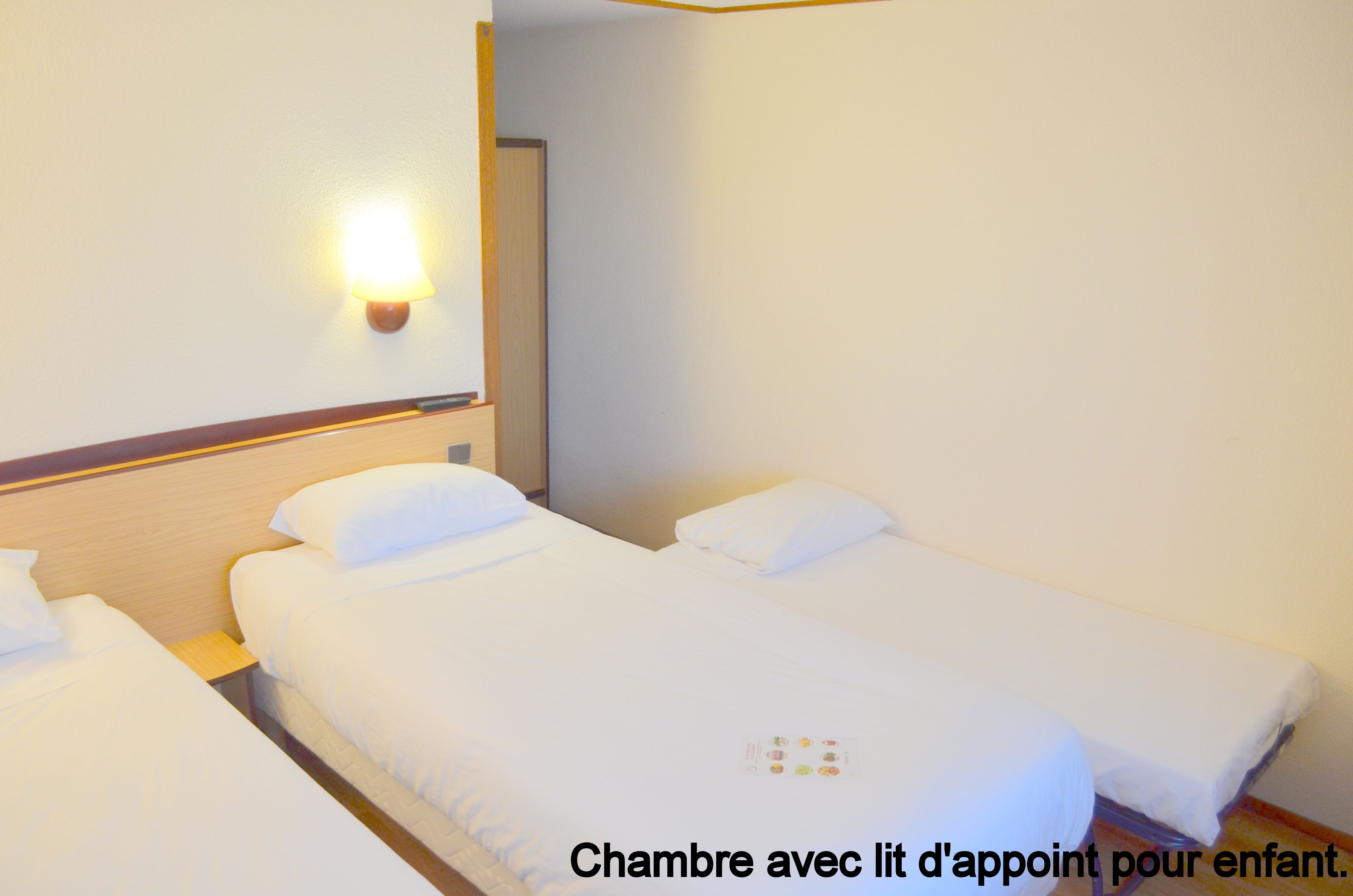Quarto de hotel com duas camas, uma mesa de cabeceira e uma luminária fixada na parede.