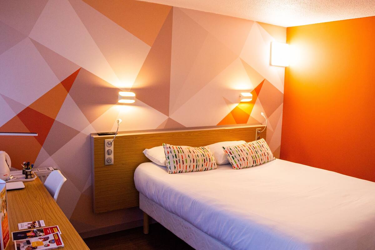 A hotel room with a bed, bedside table, lamp, and geometric-patterned wall.