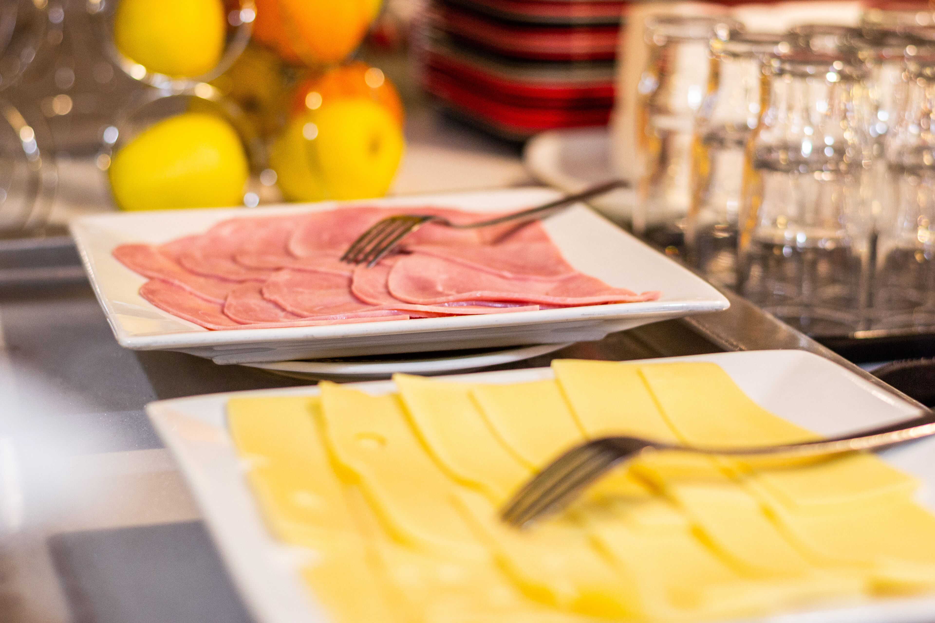 A buffet table with neatly arranged plates of sliced ham and cheese.