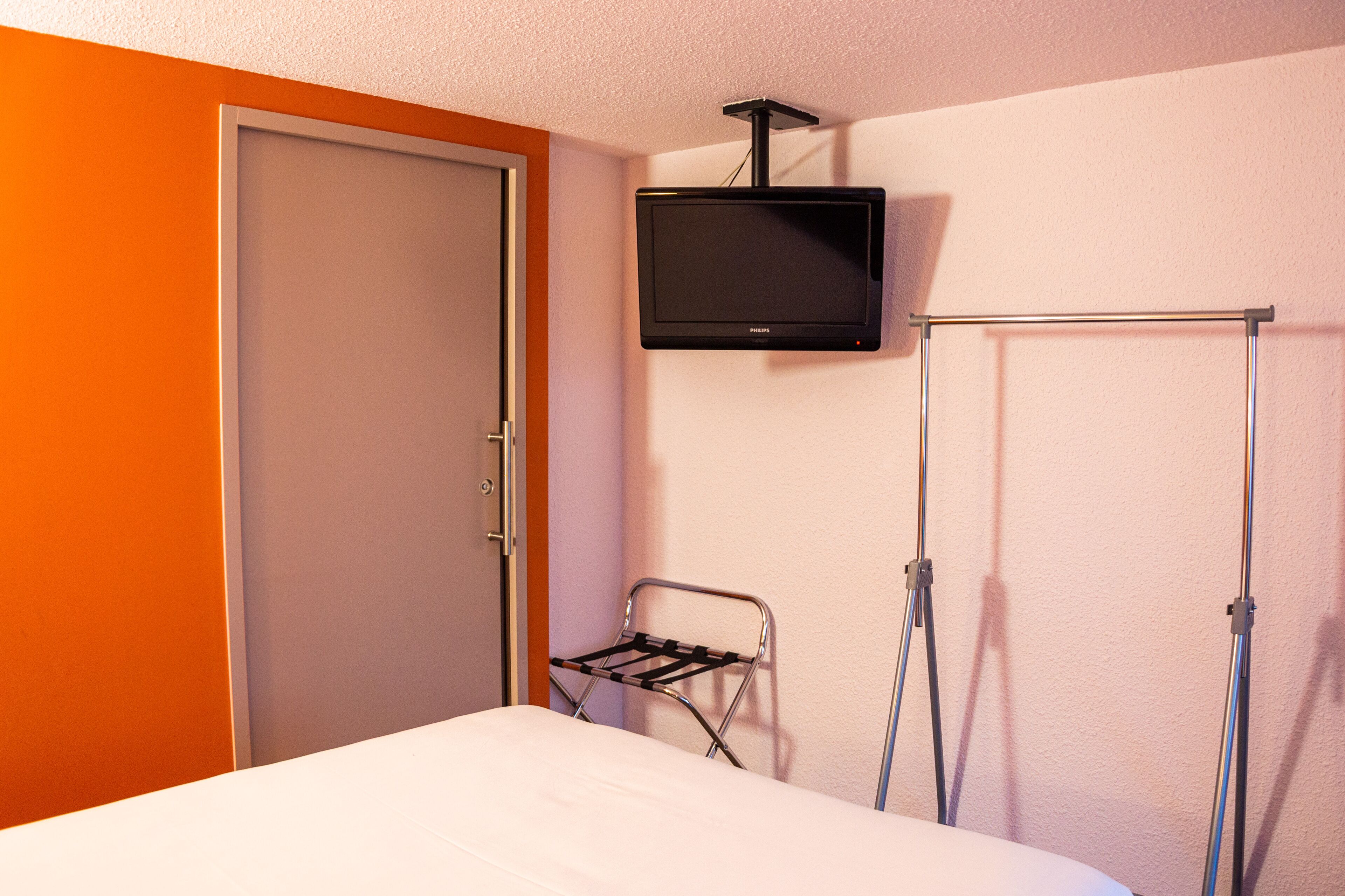 A hotel room with a bed, a television mounted on the wall, a drying rack, and a wardrobe.