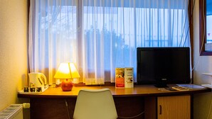 Habitació d'hotel amb escriptori, làmpada, televisió i finestra amb cortines.