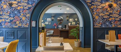Restaurante com papel de parede floral azul, mesas e cadeiras de madeira.