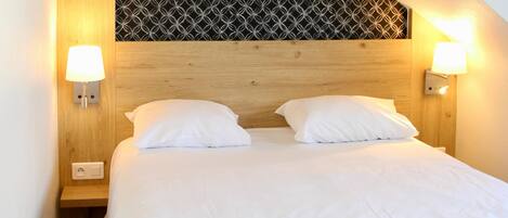 A neatly made bed with two pillows, a wooden headboard, and two wall-mounted lamps.