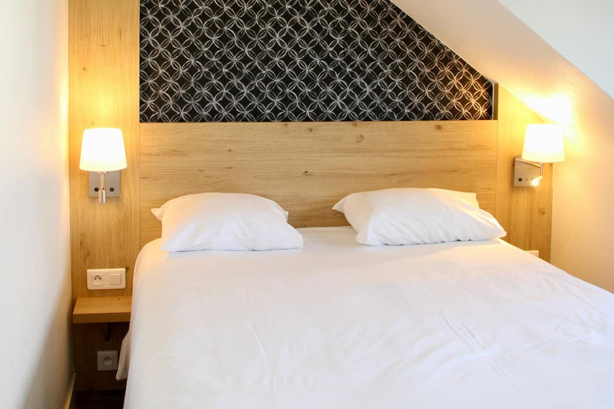 Un dormitorio con cabecera de madera, dos lámparas de noche y un papel tapiz estampado.