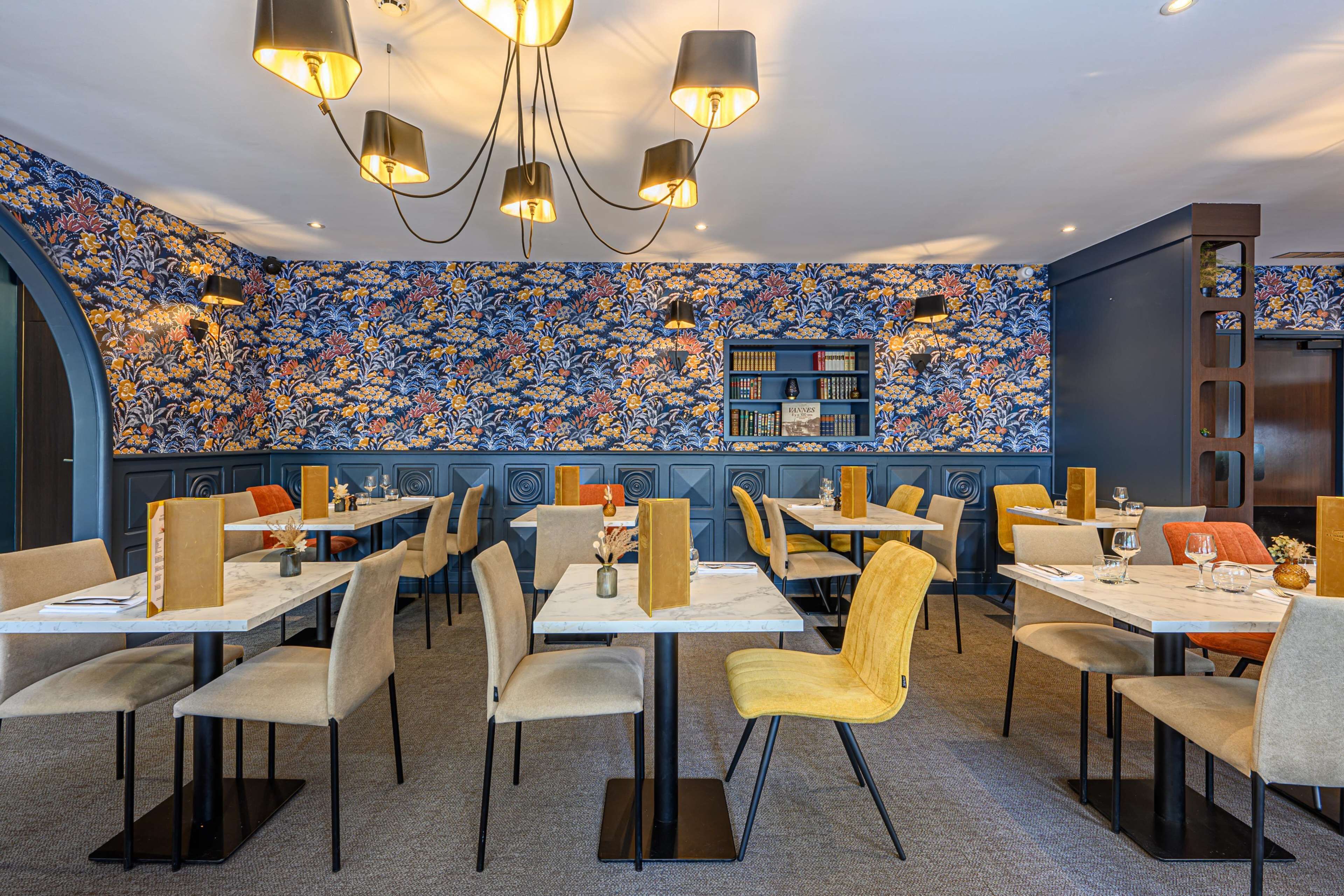 Een restaurant met een behang met patroon, tafels met stoelen en hanglampen.